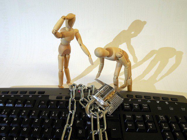 Wooden figures unlocking padlock and chain around a keyboard