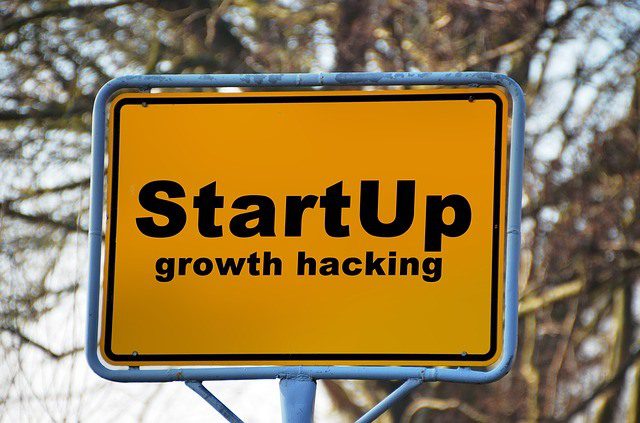 Yellow street sign that reads Startup growth hacking