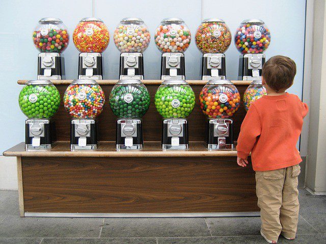 Little boy standing in front of two shelves with gumball machines of various colors