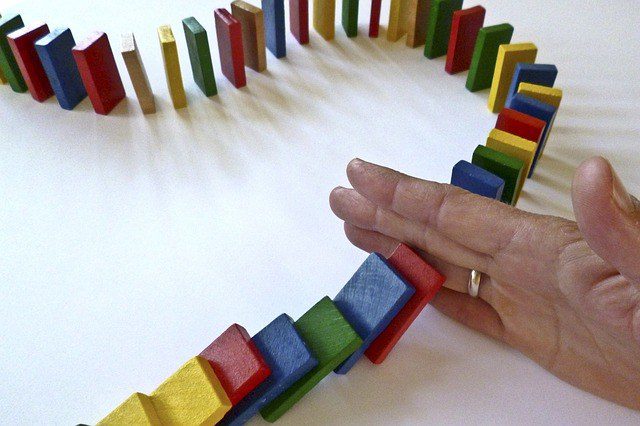 multi-colored wood dominoes in a line falling down, hand stops dominoes in the middle