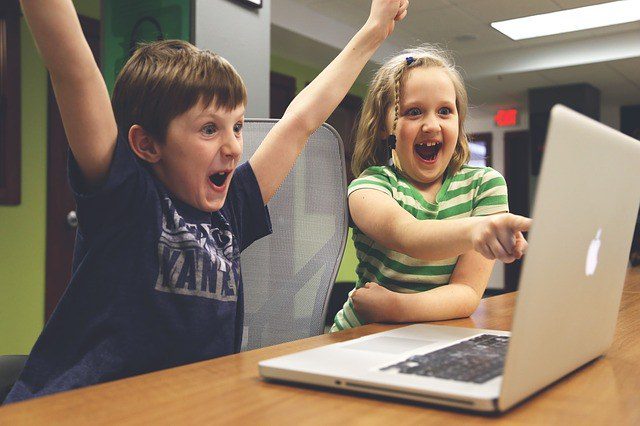 2 children playing on a laptop excited about what they are playing