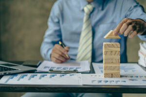 A man working on statistic reports and building a wooden house representing a firm foundation.