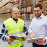 Two men in a distribution warehouse looking at ai automation software on a tablet since they invested in ai automation consulting for distributors.