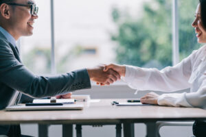 A business man is shaking the hand of a woman. He hired a great talent because his company got the help of AI talent acquisition consulting.