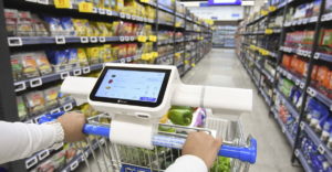 Woman pushing grocery cart down a food aisle with an AI interface on cart. This store is honing their retail strategy with generative AI