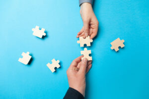 Two puzzle pieces being put together by two people. Representing what it's like when a business finds a great ai consulting firm partner.