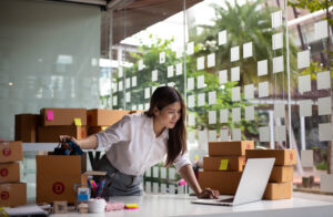 A small business leader looking at her computer with many packages around her. Her business grew so much after reading the ai consulting practical guide for small business leaders.