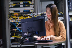 Young Asian woman in server room on computer behind the scenes of this year's AI consulting trends.