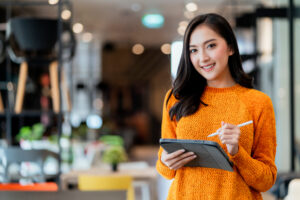 smart confidence asian female startup entrepreneur at her coffee shop using one of the top AI tools for small businesses to increase efficiency.