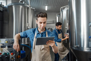 Smart factory, modern brewery management and craft beverage worker using an AI tool for small businesses on his tablet device.