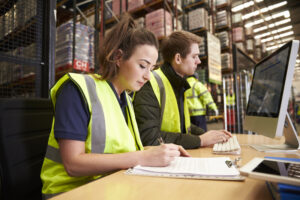 Woman and man using a computer and AI to enhance warehouse operations. One of many logistics AI use cases.