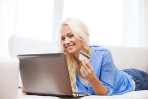 woman lying on couch with a lap top and a credit card smiling because of the added security that comes with generative ai in banking.