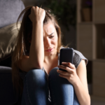 a teenage girl looking at her phone anxiously. She could use some AI in mental health benefits.