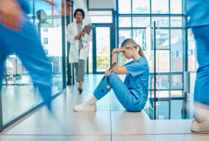 A nurse stressed out sitting on a hospital floor as people walk by.