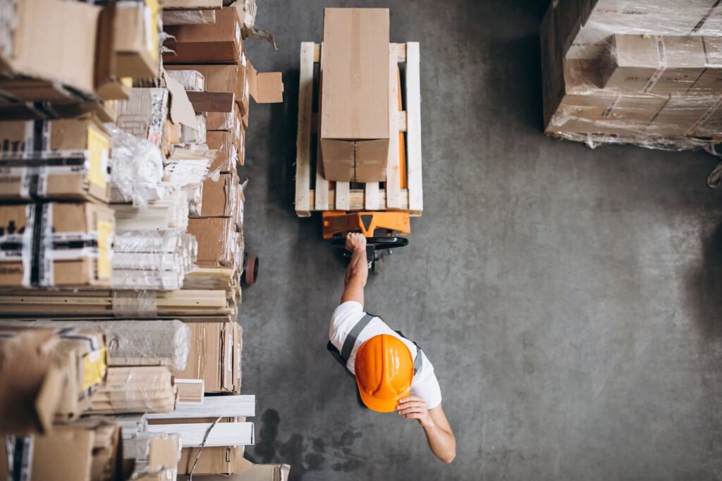 Worker in hard hat moving a pallet of boxes through a warehouse aisle